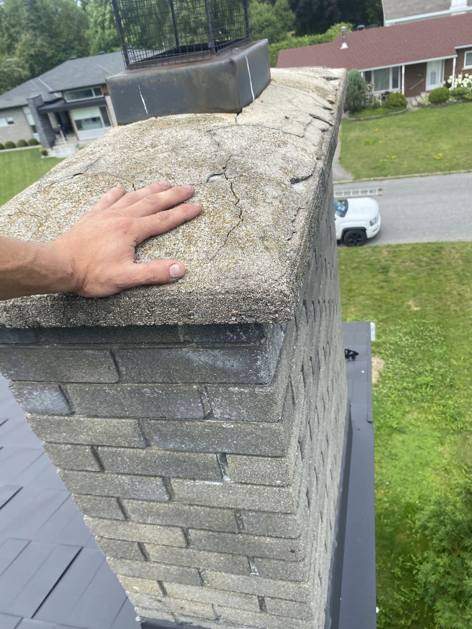 A hand resting on a cracked, deteriorating chimney crown