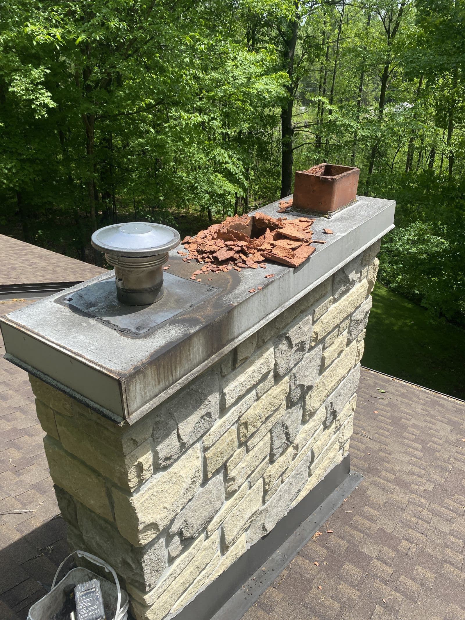 A damaged flue tile and rusted cap on a stone chimney, before repair